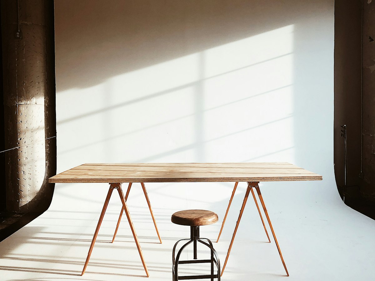 A wooden trestle table and stool in a sunlit, empty studio