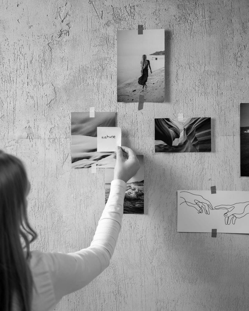 A person seen from behind pinning photographs to a textured mood-board wall