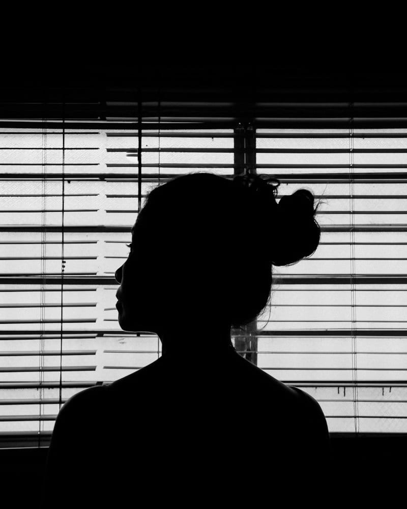 Silhouette of a person standing in front of sunlit window blinds