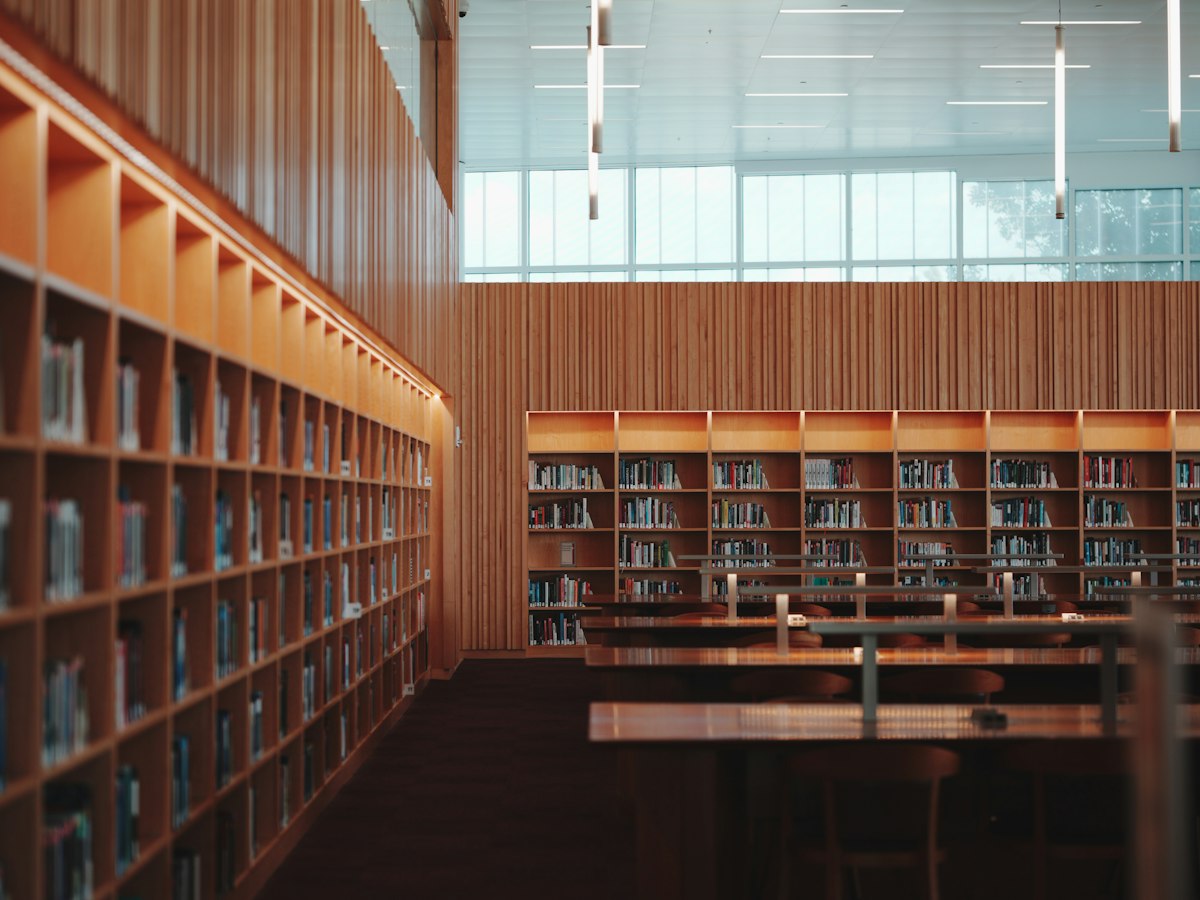 Empty library reading room with warm wood bookshelves and tall windows